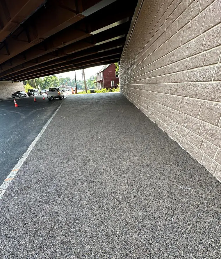 A car is parked under the bridge in an empty parking lot.