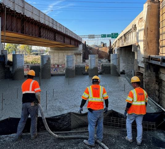 Three construction workers are working on a bridge.